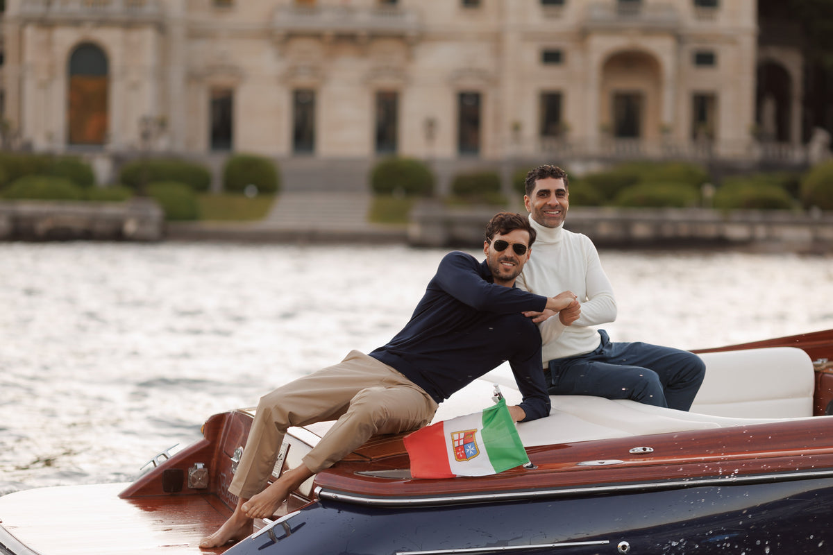 Two models in navy polo and cream turtleneck on Riva boat at Lake Como villa